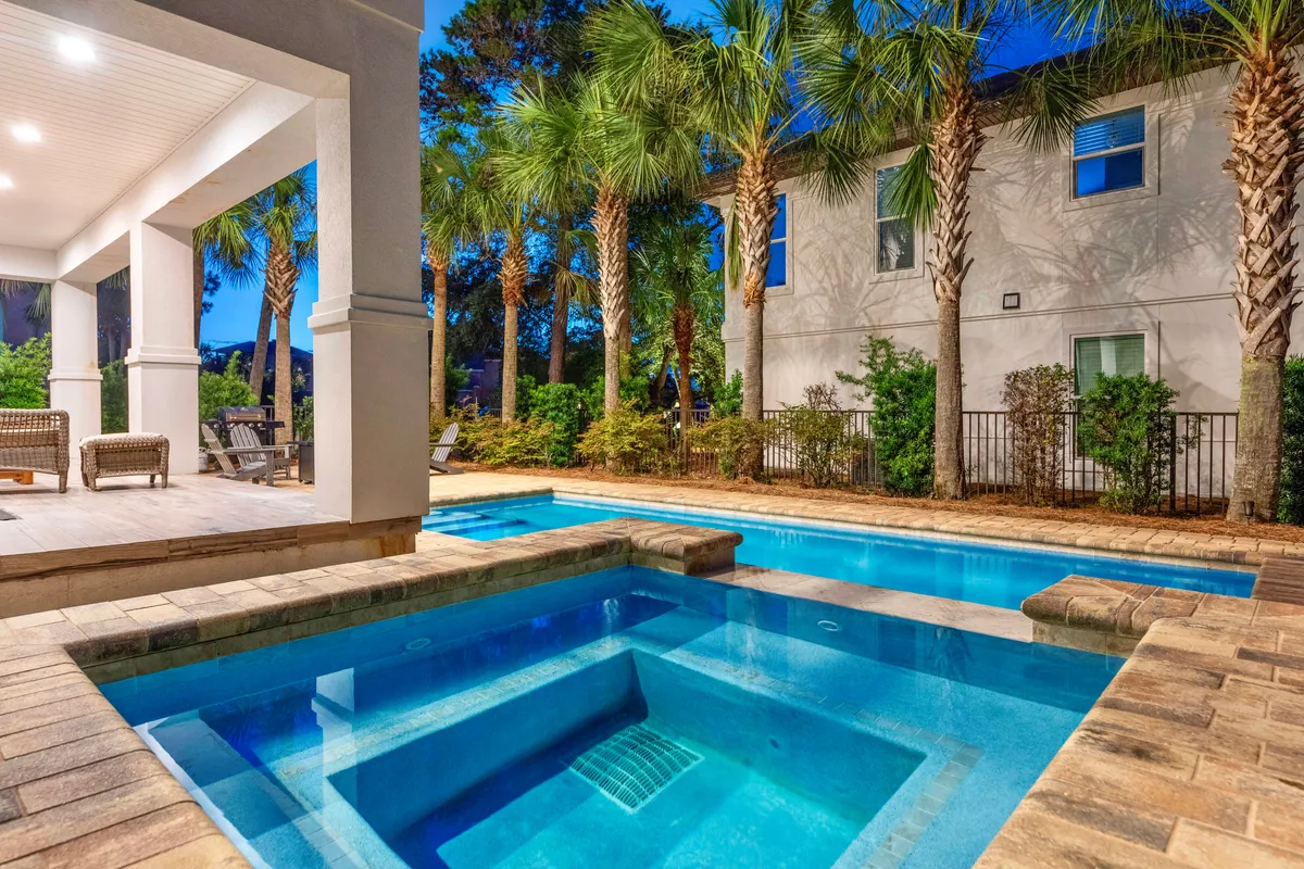 This image showcases a heated private pool and hot tub surrounded by palm trees, with a covered patio featuring inviting outdoor seating. The scene is set at dusk, creating a tranquil, exclusive atmosphere.