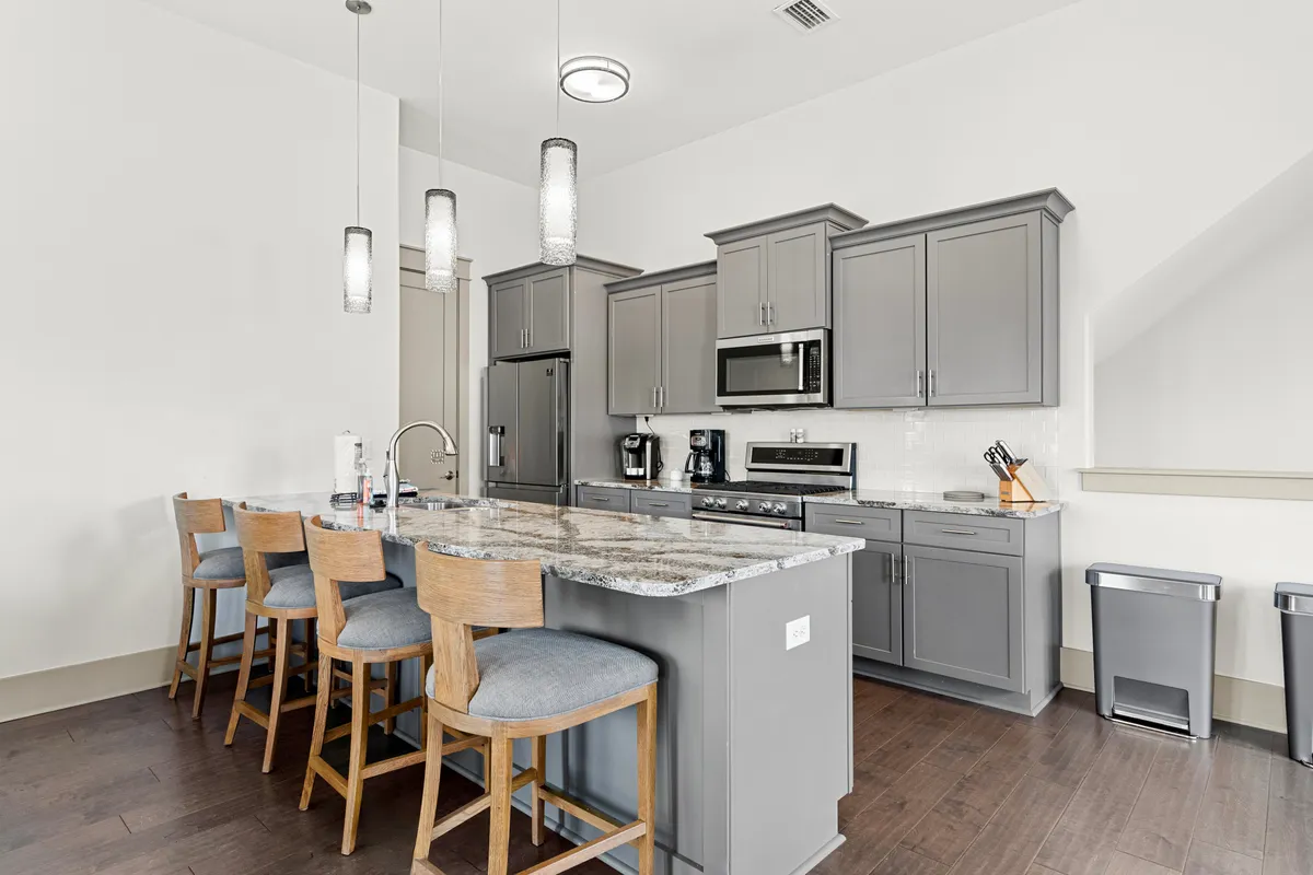 A stylish, modern kitchen with a large granite island, gray cabinetry, stainless steel appliances, and pendant lighting. The island invites casual breakfasts or coffee chats, while the open layout encourages interaction during meal prep or entertaining.