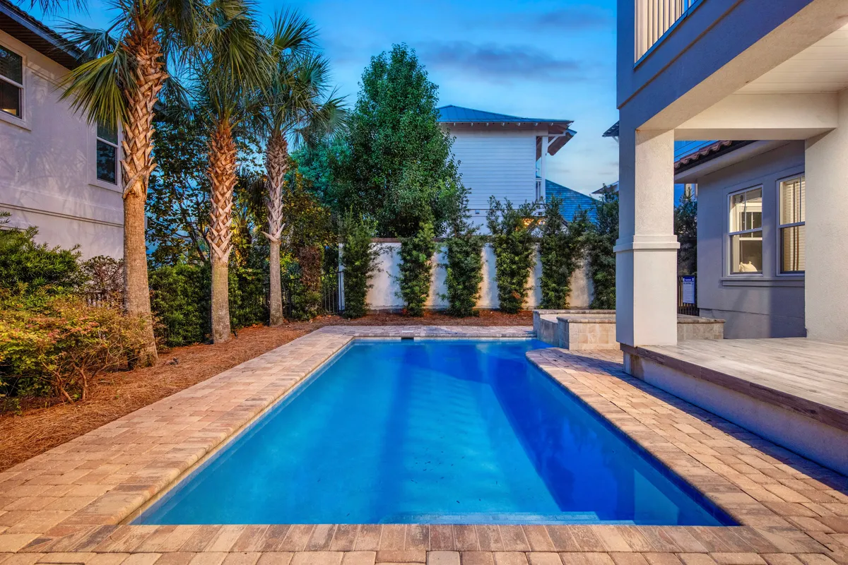 This image showcases a private heated pool surrounded by lush greenery, tall palm trees, and a modern covered patio area. The blue water and manicured landscaping create a luxurious, inviting outdoor retreat, ideal for relaxation or small gatherings.