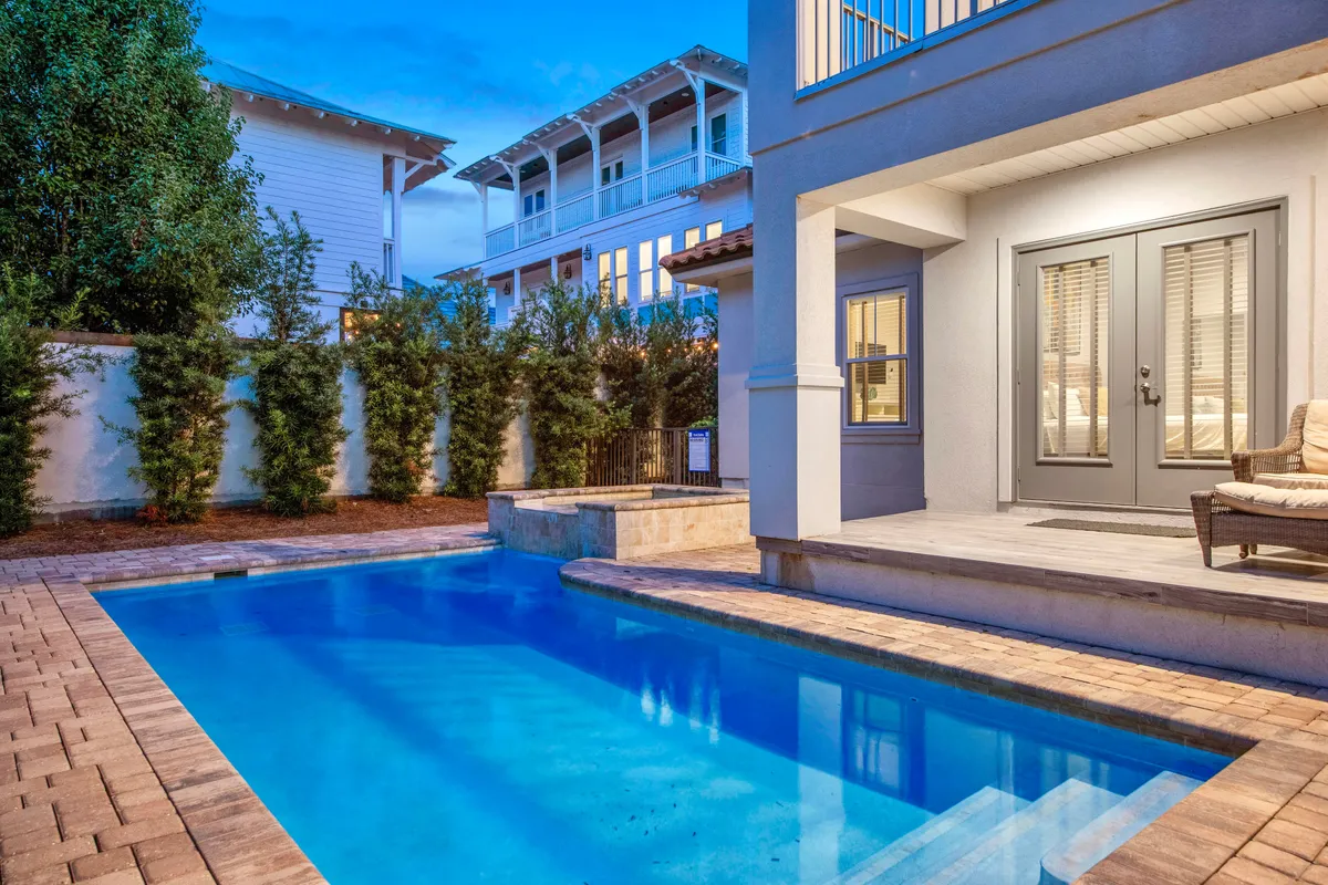 An inviting private heated pool and modern outdoor seating area, framed by lush greenery and tall palm trees, create a tranquil setting for swimming, lounging, or socializing. The stylish architecture hints at the upscale nature of the property.