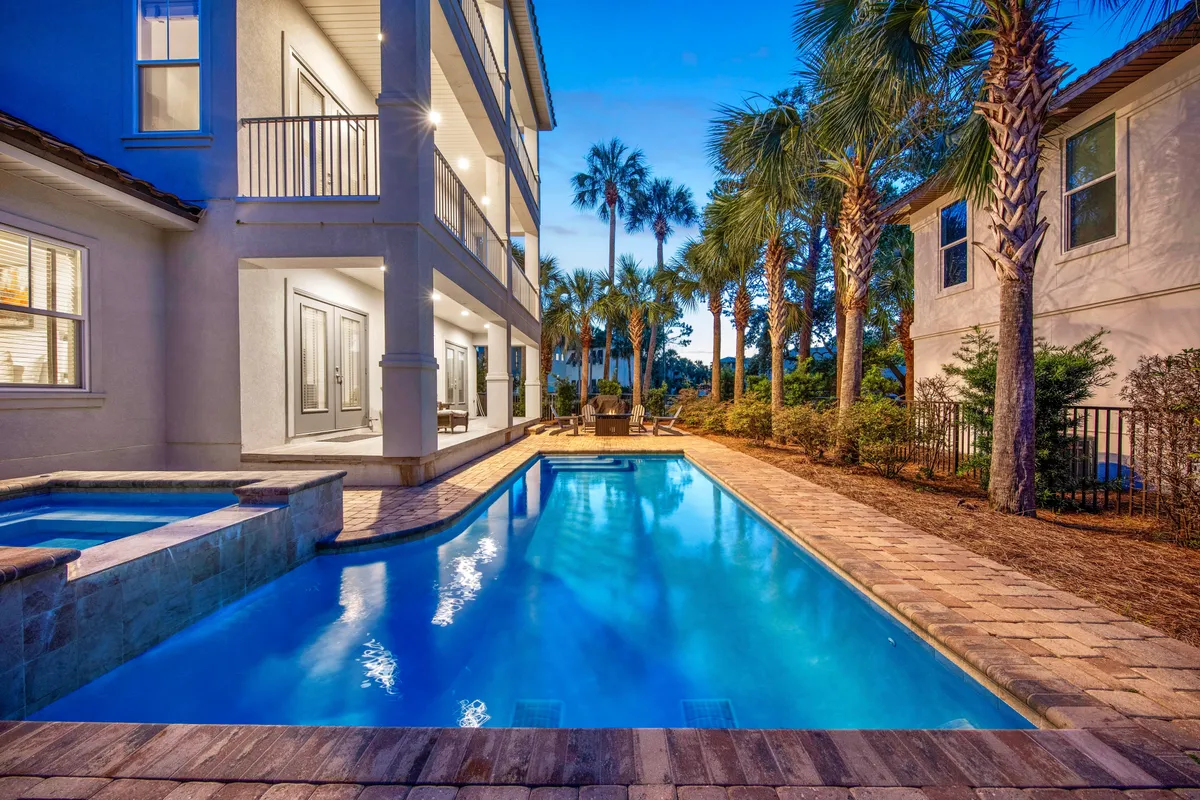 This image showcases a private heated pool and hot tub/spa area surrounded by tall palm trees. The poolside seating area and covered porch are visible, evoking a tranquil, upscale atmosphere perfect for relaxation or group gatherings. The lush landscaping and inviting water features create the sense of a personal tropical oasis within a gated community.